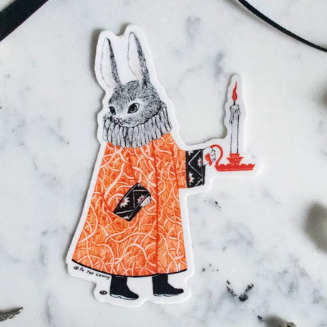 A mysterious rabbit dressed in a patterned robe carries a glowing candle through the night. This whimsical illustration blends folklore and magic, making it a perfect sticker for anyone who loves enchanting details. Printed on durable white vinyl, this sticker is waterproof, UV-proof, and made to last — ready to decorate laptops, journals, bottles, and more.