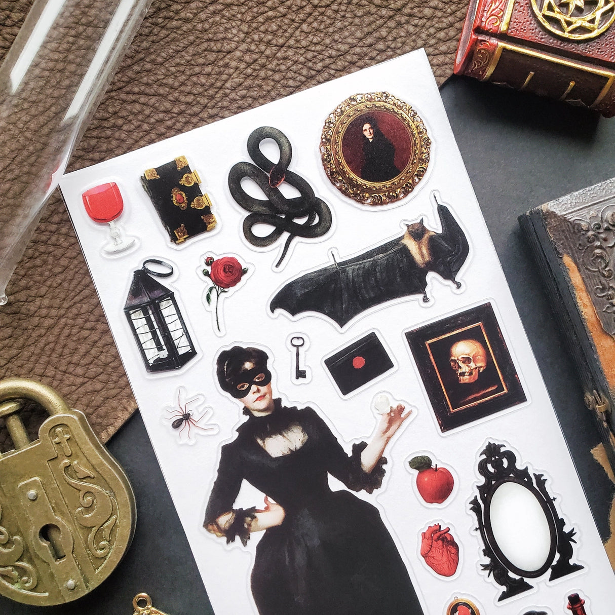 🕯️🦇 Step into a shadowy parlor of vintage gothic charm with this hauntingly elegant sticker sheet. From mysterious masked figures and candlelit curiosities to ravens, roses, serpents, and forbidden tomes, every piece feels plucked from an old-world cabinet of wonders. Perfect for adding a touch of dark romance, eerie beauty, and timeless intrigue to your spreads and creations.