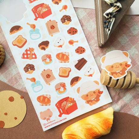 🧺🍯 Pack your blanket for the coziest little picnic! This darling sheet by @yomihonei is filled with flaky croissants, chocolatey buns, chunky cookies, golden loaves, buttery toast, and jars of honey all nestled on a gingham spread. With an adorable bear friend busy filling baskets and tying up tasty treats, it’s a kawaii afternoon of sunshine, crumbs, and cuddly bakery bliss. These stickers will add a drizzle of honeyed happiness wherever you stick them!

Art by: @yomihonei

Top Coating: None
Adhesive Lay