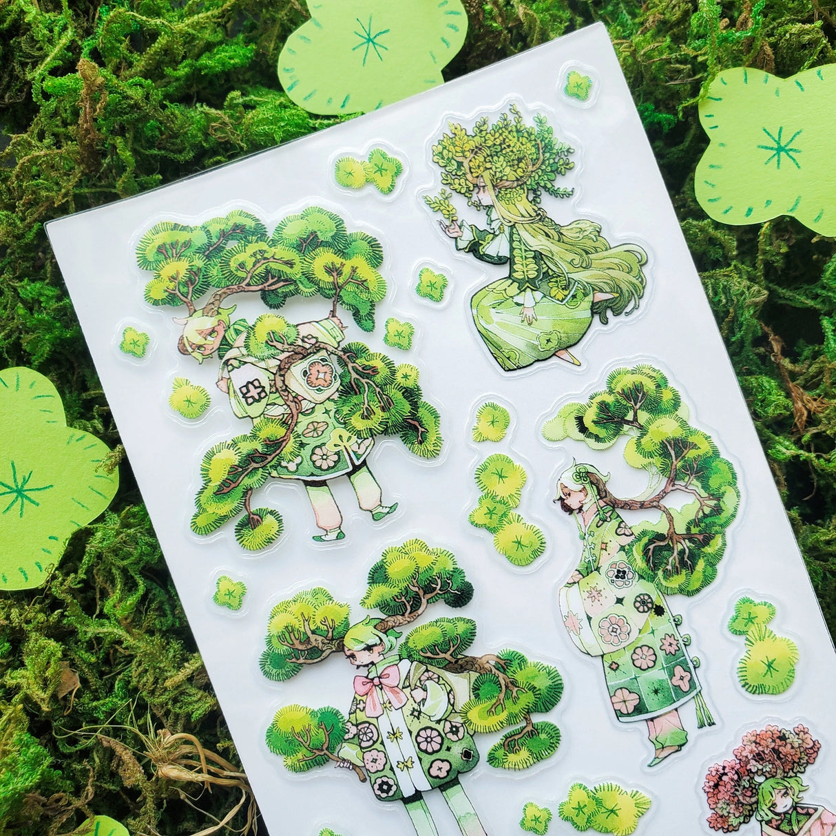 🌳🍃 Get ready to branch out with @maruti_bitamin’s bonsai beauties and leafy legends! These stylish forest guardians rock living tree crowns, flowing robes, and nature magic like it’s the hottest green trend of the season. Rooted in charm and bursting with botanical flair, this set is ready to sprout some serious wow on your pages!

Art by: @maruti_bitamin

Top Coating: None
Adhesive Layer: PVC (plastic)
Backing Layer: Clear PET
6.69" x 3.54".
Weight - 0.03lbs.
1 sheet included &nbsp; &nbsp;