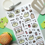 🍔🐸 Say hello to the cutest chef in town! @keziacreations’ adorable little froggy is busy in the kitchen flipping patties and serving up smiles. From sizzling burgers to crispy fries and fizzy drinks, this tiny chef is here to make your heart (and tummy) hoppy.

Art by: @keziacreations

Top Coating: None
Adhesive Layer: Paper
Backing Layer: Clear PET
6.69" x 3.54".
Weight - 0.03lbs.
1 sheet included&nbsp;