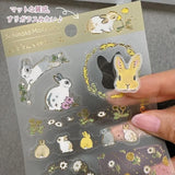 A sticker sheet with golden touches featuring rabbits surrounded by nature and blooming flowers is here to add both adorable and elegant touches to your journal pages