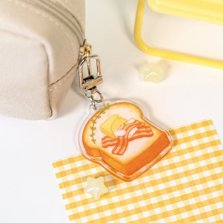 The Sweet Dreams keychains feature Muffin Corner characters sleeping on top of some of their favorite foods. Devyegg is sleeping a warm piece of toast after a late night of working.

Details:

Approximate Dimensions: 1.6” x 1.8” (4.1cm x 4.4cm)&nbsp;
Material: Acrylic
Double-sided
Comes with 1 Keychain