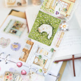 Step into a world where nature and comfort collide. Our Summer Café Wide Tape transforms your stationery into a bustling garden bistro, teeming with life, blooming flowers, and the true owners of the cafe: the cats.

This whimsical design weaves together the architecture of charming coffee shops with the wild beauty of summer florals. Nestled among the potted plants and open doors, you’ll find hand-painted cats exploring, sleeping, and playing.&nbsp;

