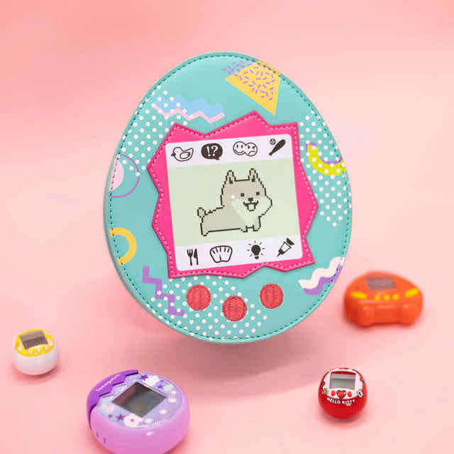 Throwback to the Tamagotchi days! Did you own a virtual pet back in the day? If not, do not worry, we got you covered. Available in cat or dog.  Features a zipper closure and adjustable strap.

Dimensions: 7.25” x 3” x 8.5”