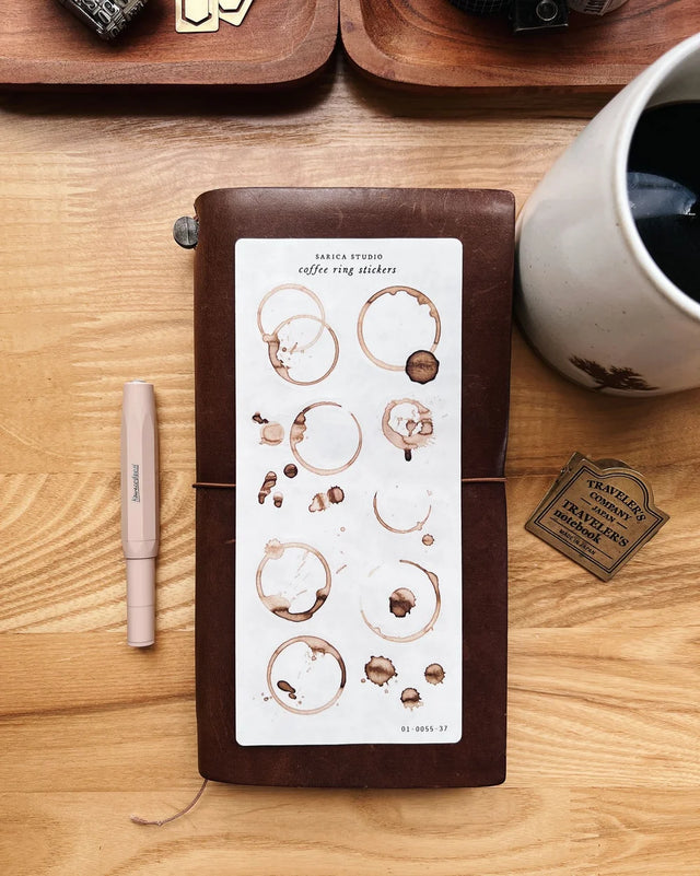 Notebook with coffee ring stickers on a wooden surface with a pen and mug.